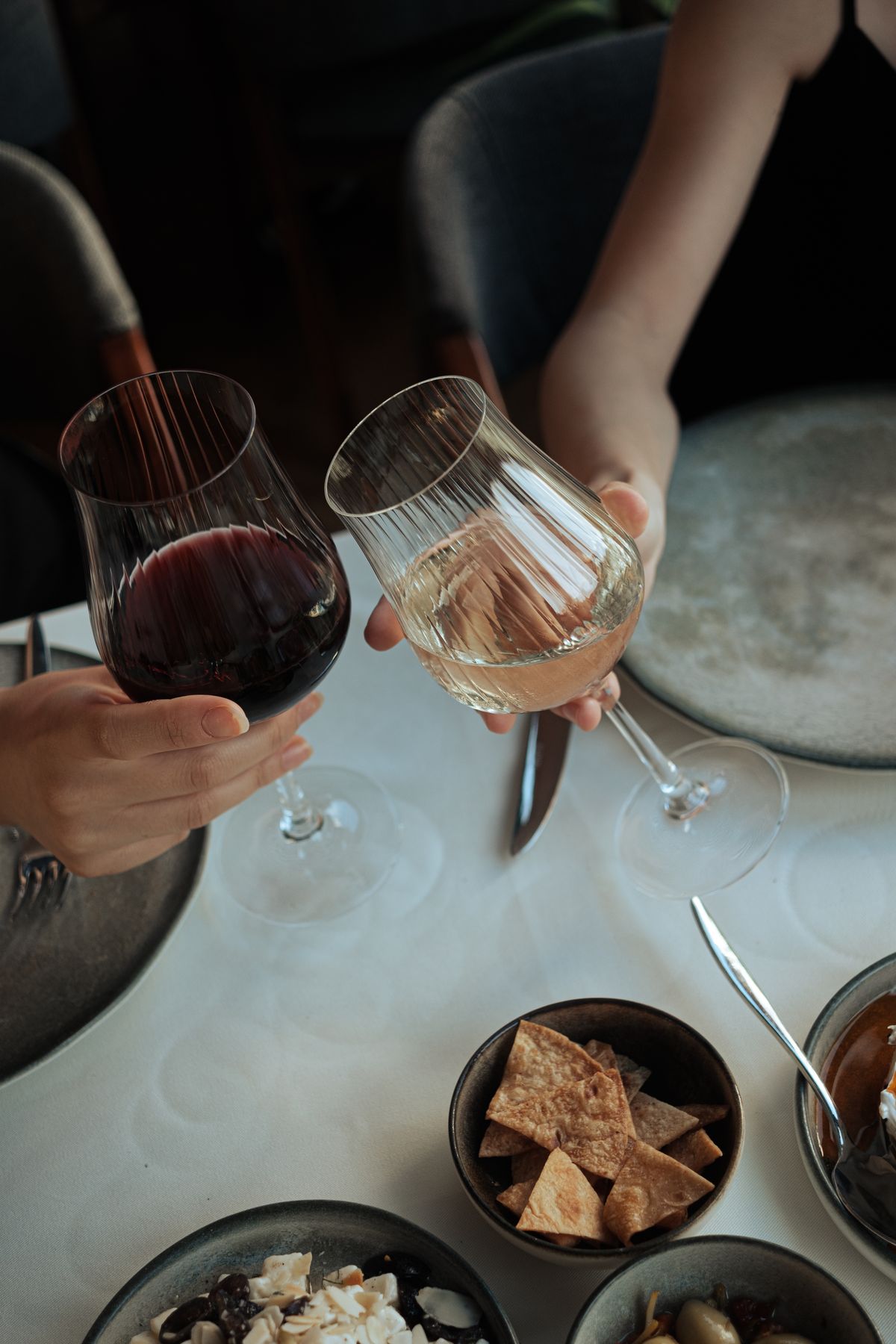 Two people toasting wine glasses above a dinner table